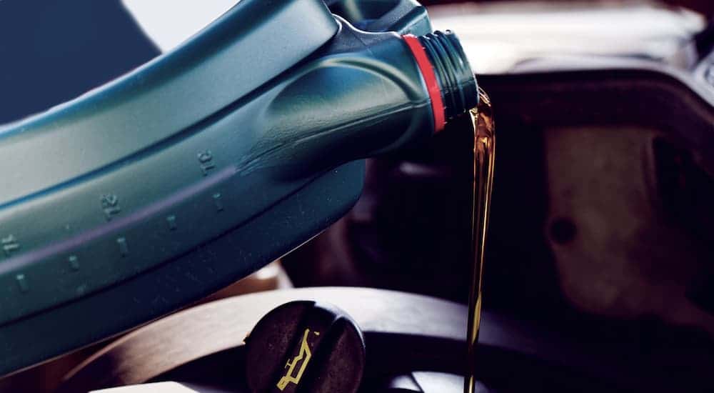 Oil is pouring with the engine oil cap visible. Changing oil can be part of a quick lube.