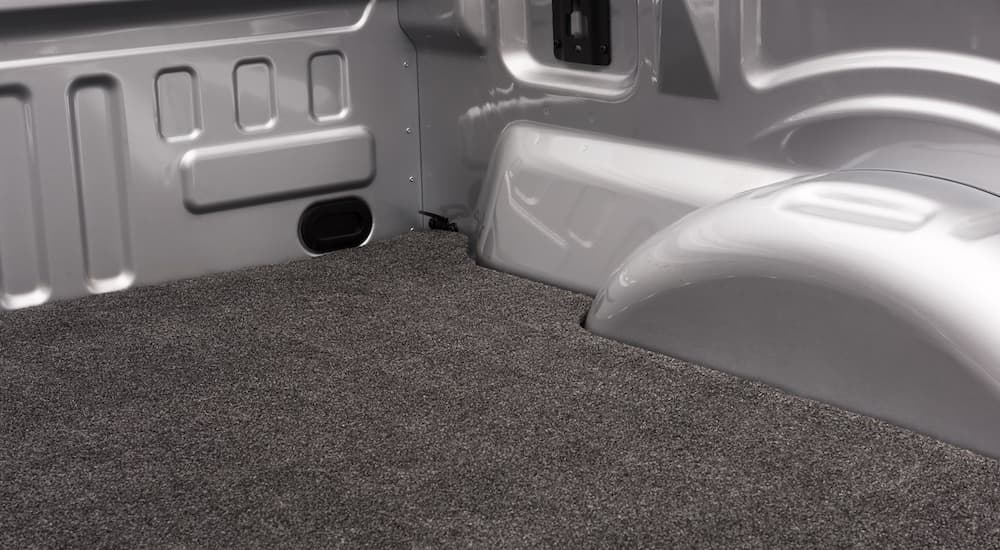 A grey bed rug style truck bed liner is shown in a close up on a silver truck.