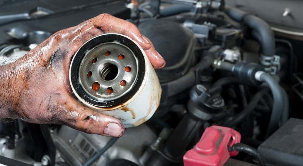 A hand is holding a used oil filter over a motor during an oil change.
