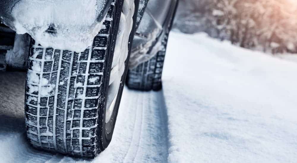 A closeup of snow tires with tracks in the snow is shown.