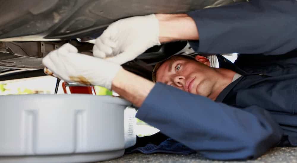 A man is under a car draining oil during an oil change.