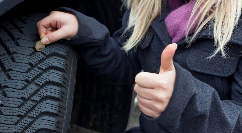 A woman is giving a thumbs up while checking her tires with a coin.