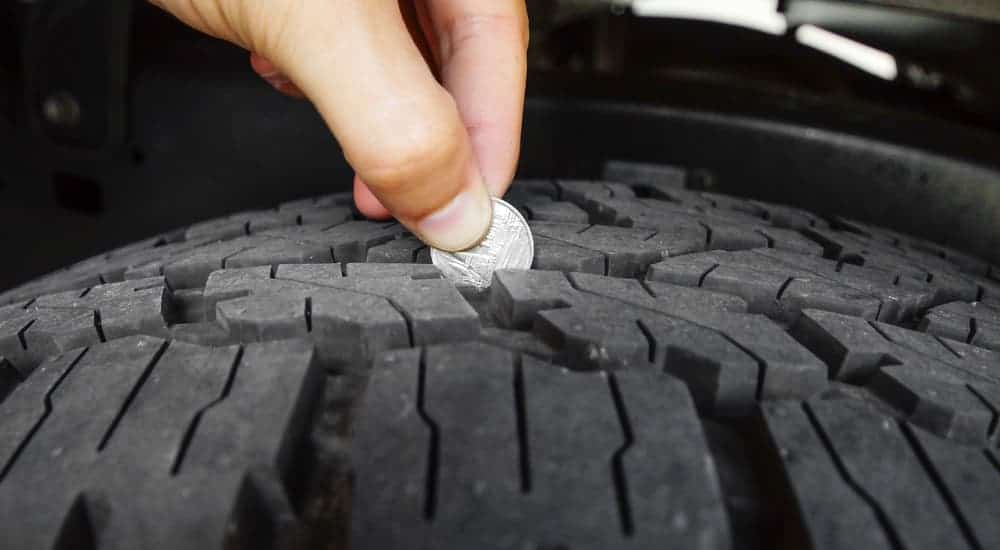 A closeup of a coin being used to check tire tread is shown.