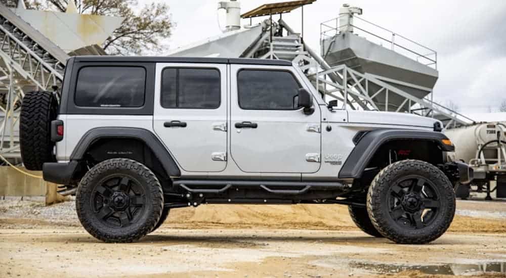 A silver Jeep Wrangler in a gravel pit is shown from the side with a body lift kit.