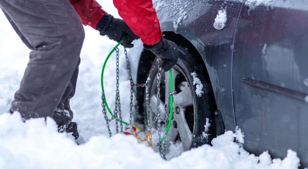 A man is putting tire chains on his car in the snow.