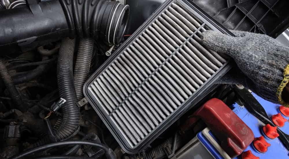A gloved hand is holding a dirty air filter over an engine.