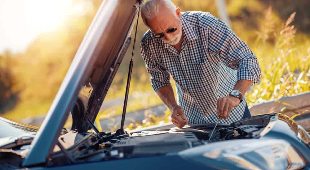 A man is under the hood checking his oil for preventative car maintenance.