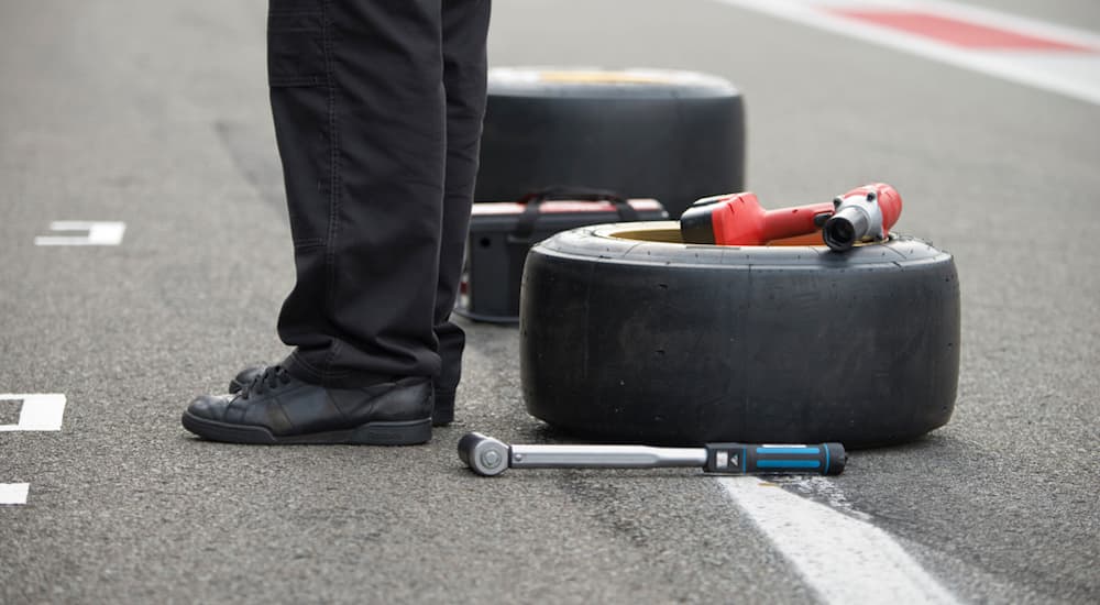 Two race slicks, not your average discount tire, are on the ground next to a pit crew member.
