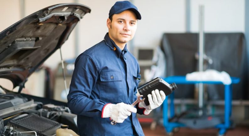 A mechanic is shown holding a bottle of oil.