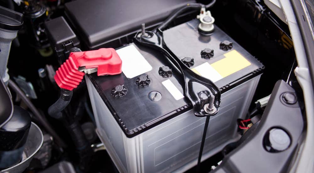 A black car battery with red and black terminal wires in the engine compartment