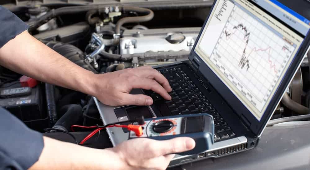A mechanic is using a diagnostic machine next to a car's engine bay.