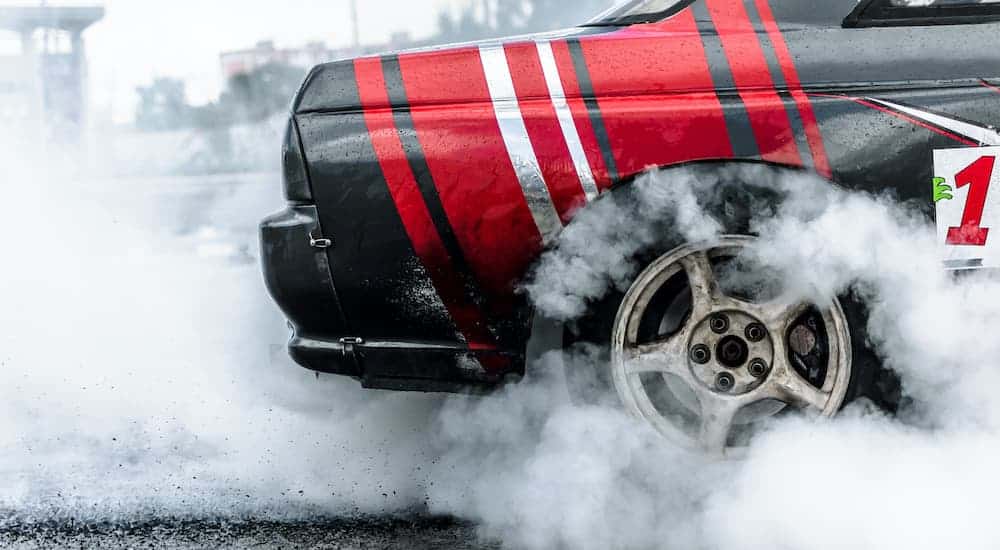 A close up is shown of the rear wheel on a track car doing a burnout.