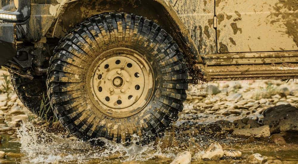 A close up is shown of an all-terrain tire driving through the mud.