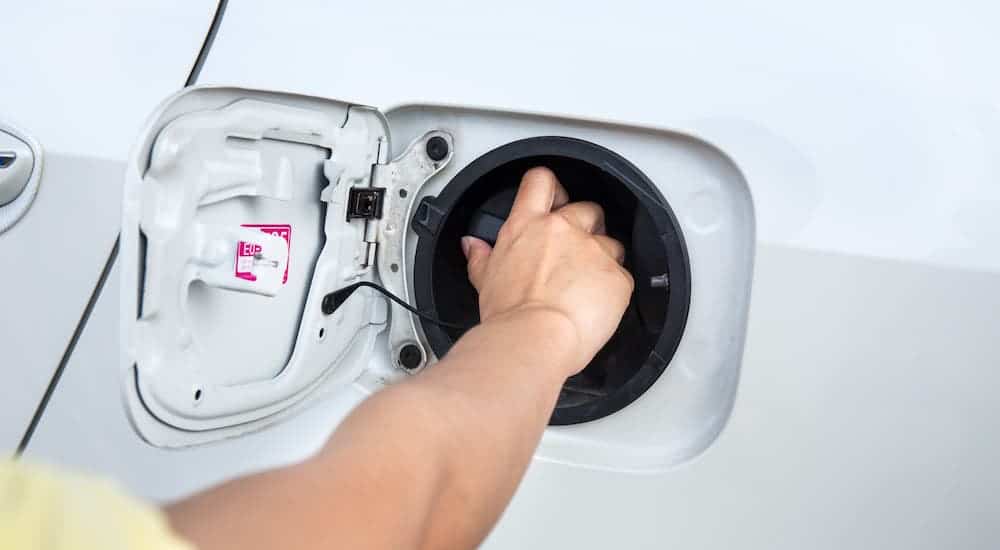 A hand is tightening the gas cap on a white car, a common cause of the check engine light.