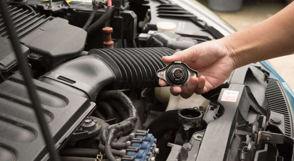 A closeup shows a hand taking off a radiator cap under a car's hood.