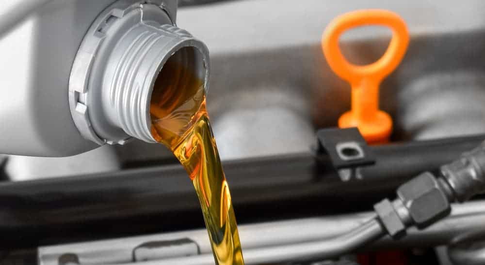 Oil is being poured from a jug in front of an engine bay.