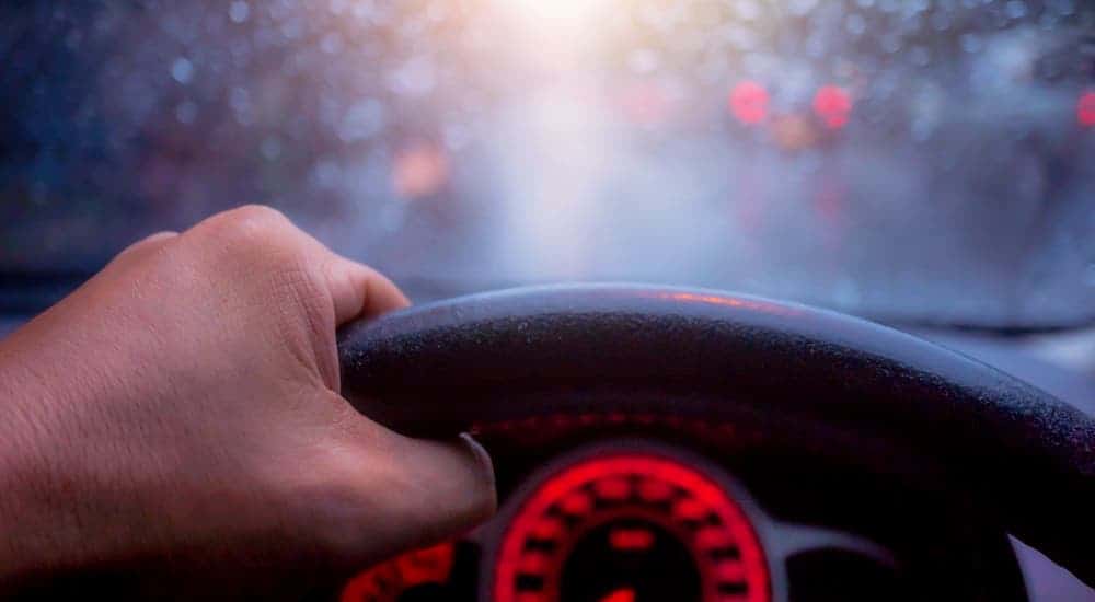 A closeup shows a hand on a steering wheel and an out of focus windshield.