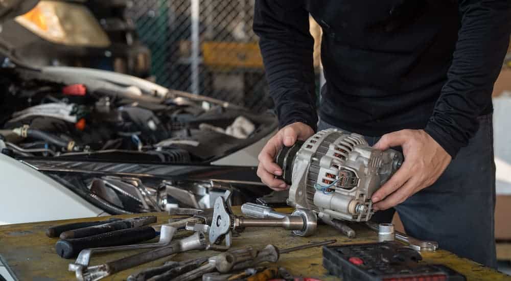 An alternator is being held by a mechanic over a table covered in tools.