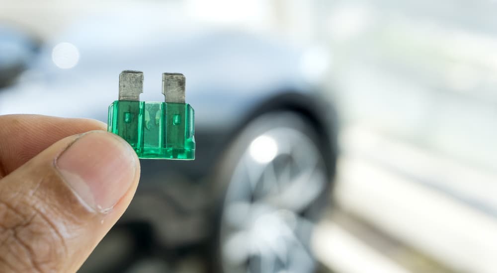 A close up is shown of a hand holding a broken green car fuse.