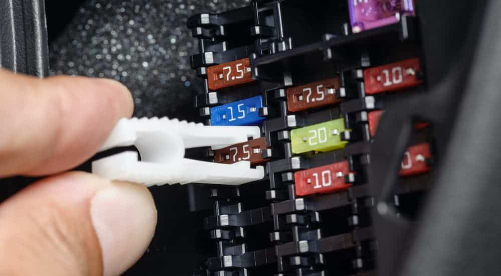 A close up is shown of someone using a fuse removal tool in a fuse box.