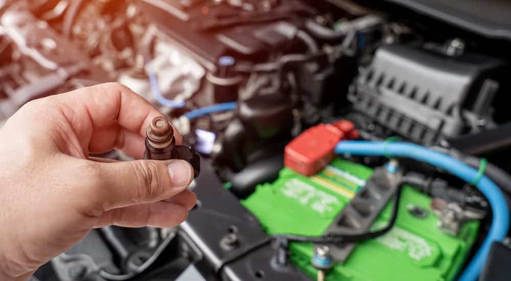 A hand is shown removing a fuel injector over an engine.