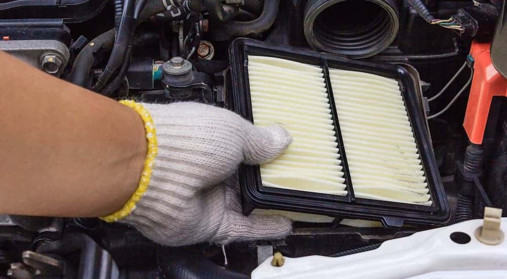 A gloved hand is holding an air filter in the engine bay of a car.