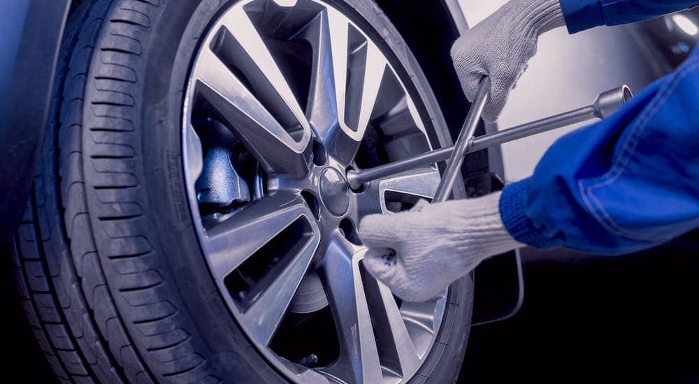 A closeup shows gloved hands using a tire iron to tighten the lug nuts on a tire.