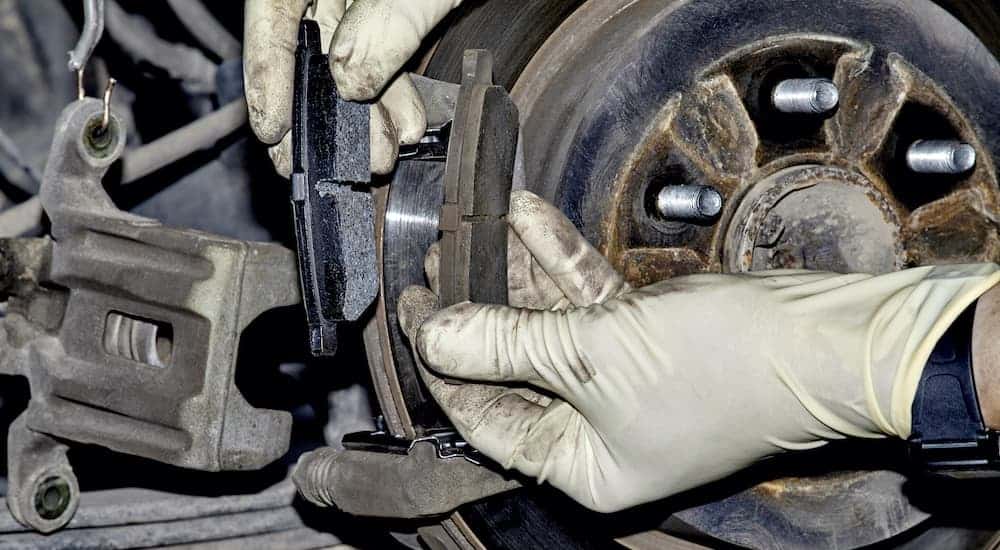 A set of gloved hands is shown holding a new and used brake pad side-by-side.