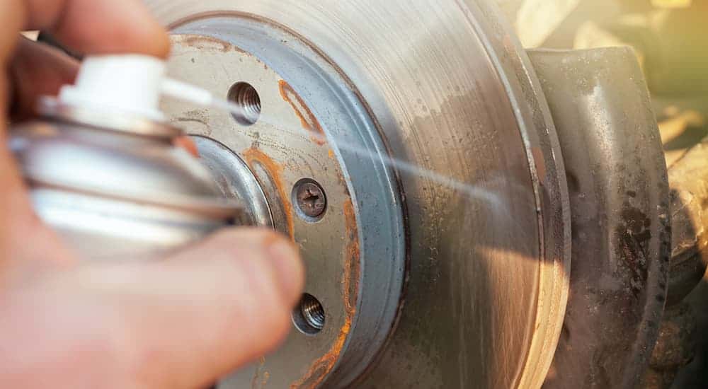 A close up shows a person spraying a cleaning agent on a brake rotor.