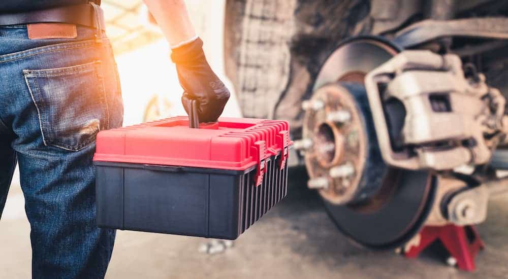 A man with a rad and black toolbox is shown approaching a vehicle that has a wheel removed.