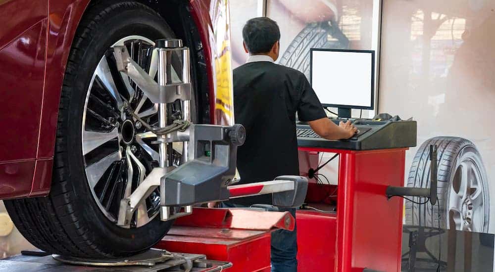 A mechanic is shown on a computer from behind while performing an alignment service on a red car on a lift.
