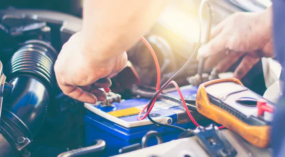 A close up shows a mechanic testing a car battery with a multimeter.