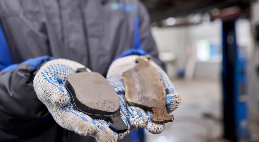 A gloved mechanic is holding two brake pads, one is used and the other new.
