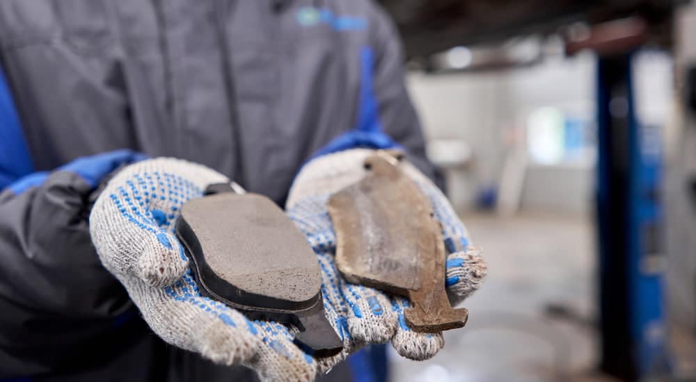 A mechanic is holding two brake pads, one is new and the other is used.