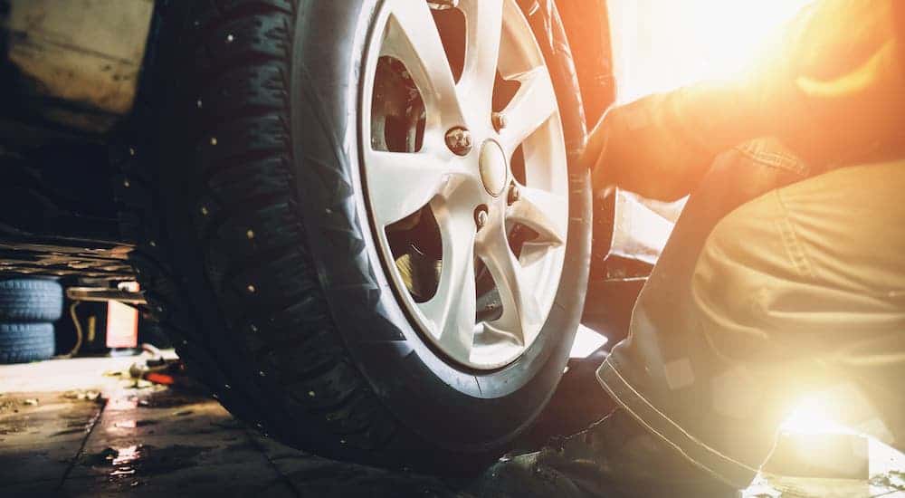 A closeup shows a mechanic putting a wheel on a car.