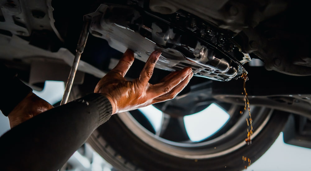 A mechanic is holding a drip pan under a car.