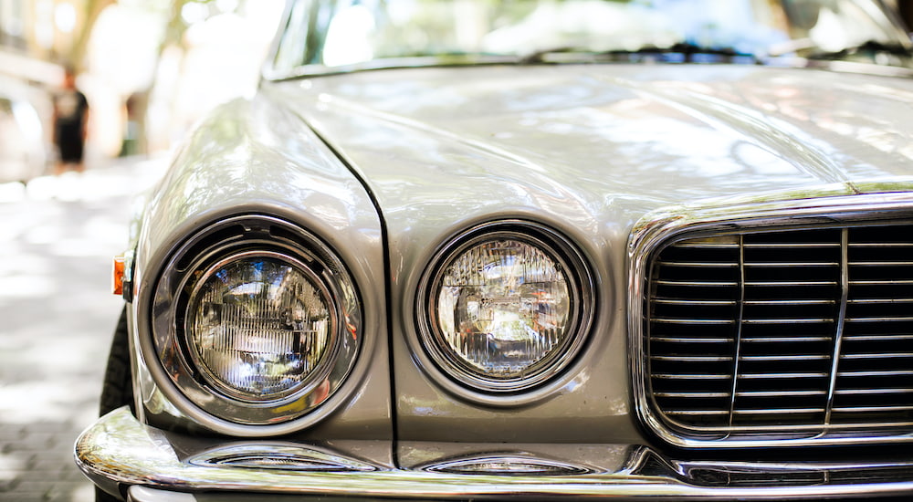 A tan vintage car shows a close up of the left hand side headlights.