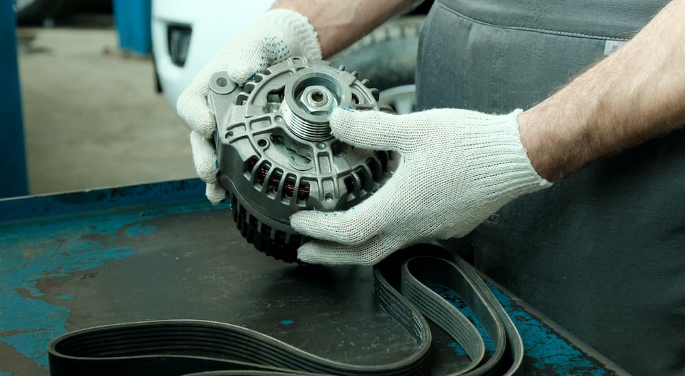 A gloved mechanic is shown holding an alternator during a Nissan service.