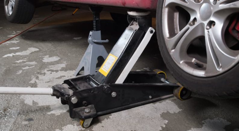 A close up shows a floor jack and jack stands being used to work on a car.
