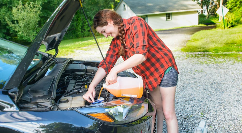 A woman is shown adding windshield wiper fluid to her car.