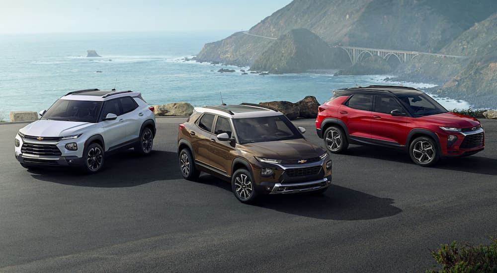 A white, a bronze, and a red 2022 Chevy Trailblazer are shown parked in front of an ocean.