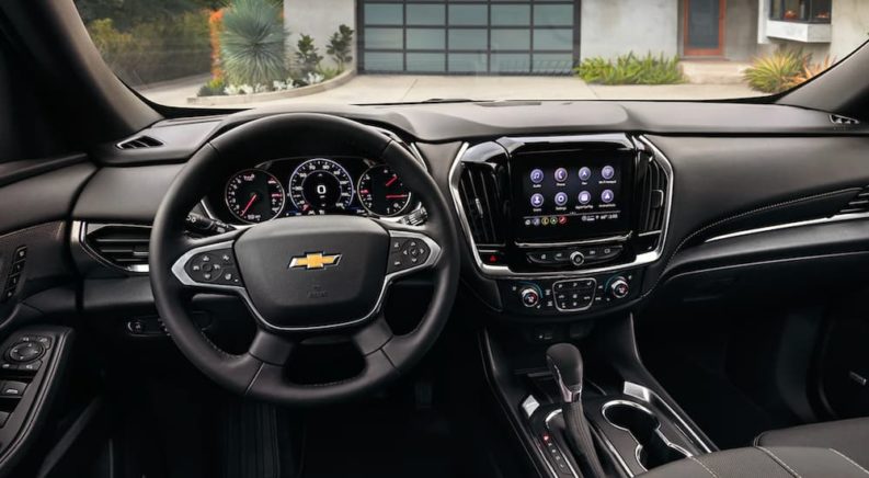 The black interior of a 2022 Chevy Traverse shows the steering wheel and infotainment screen.