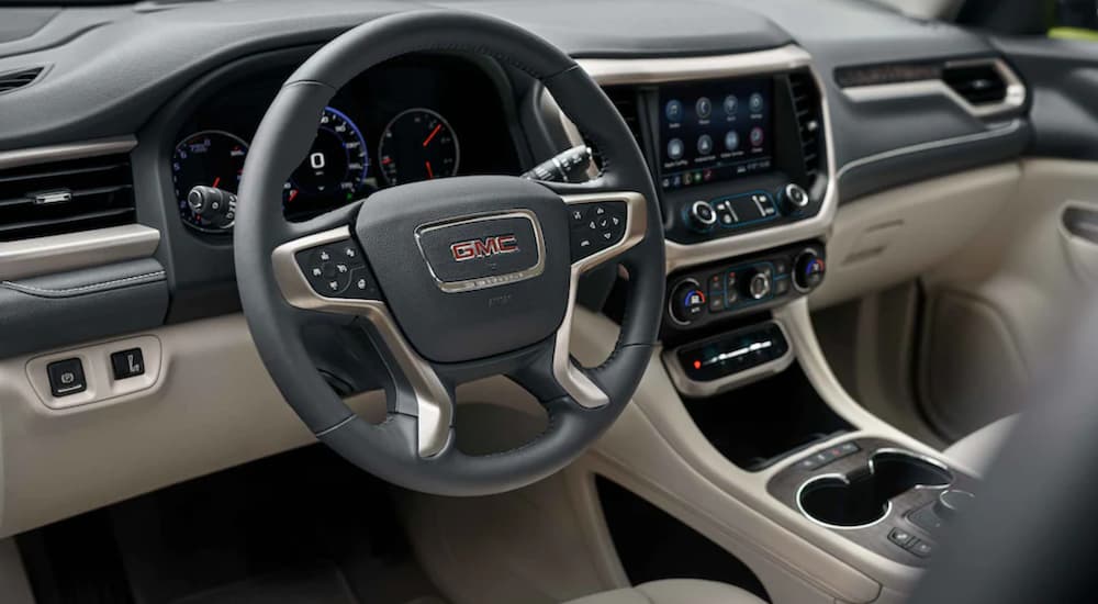 The black and tan interior in a 2022 GMC Acadia shoes the steering wheel and infotainment screen.