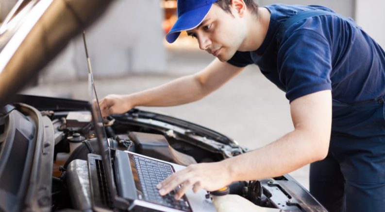 A mechanic is shown flash tuning a vehicle with a laptop computer placed on the car engine.