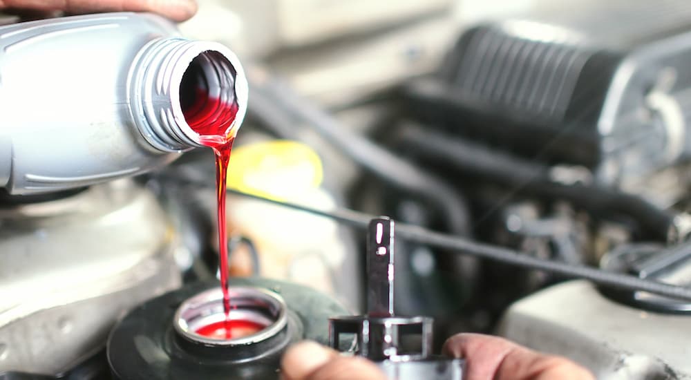 Red transmission fluid is shown being poured into a vehicle's engine.