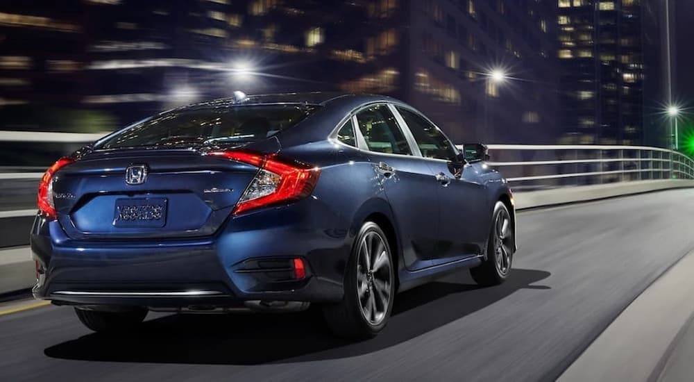 A blue 2021 Honda Civic EX is shown driving down an empty city highway at night.
