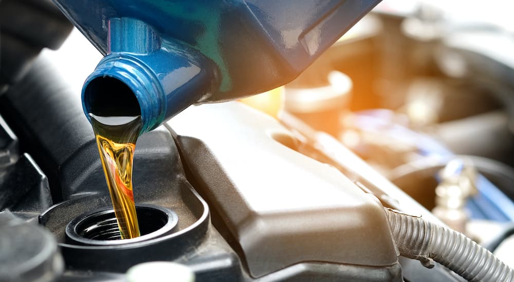 A blue bottle of oil is shown being poured into a vehicle.