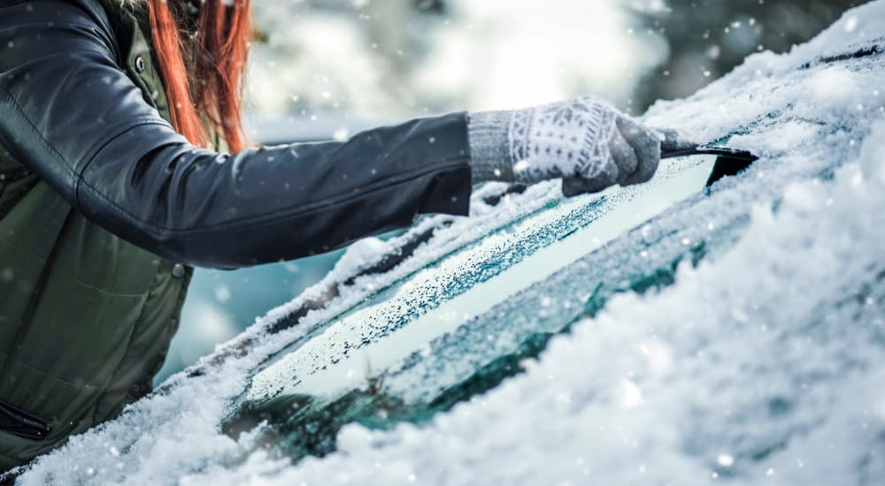 A woman is shown scraping ice off of her car's windshield.