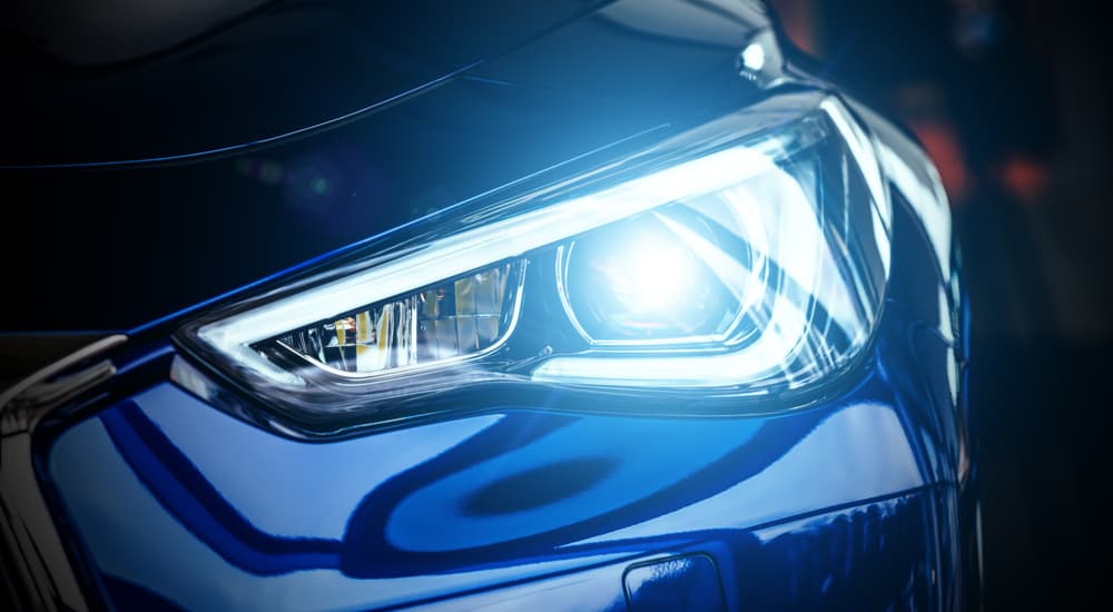 A close up shows the headlight of a blue car.
