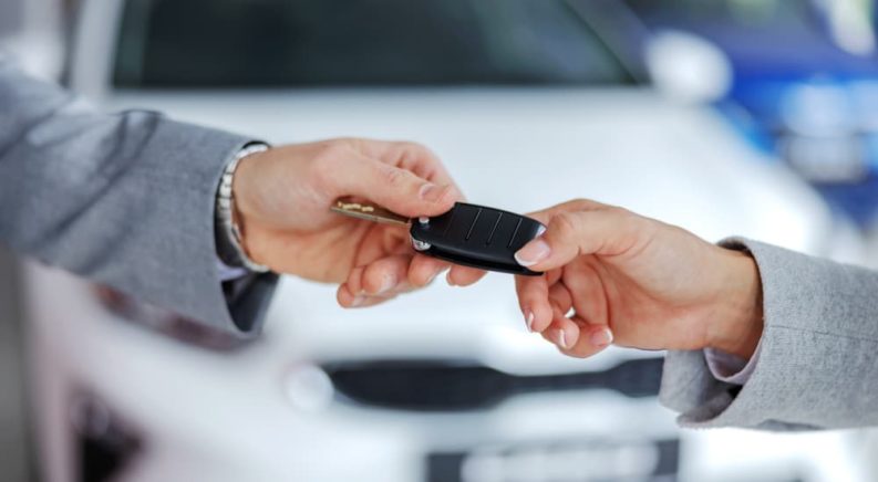 A person is shown handing a car key to a salesman after researching 'how to sell my car.'